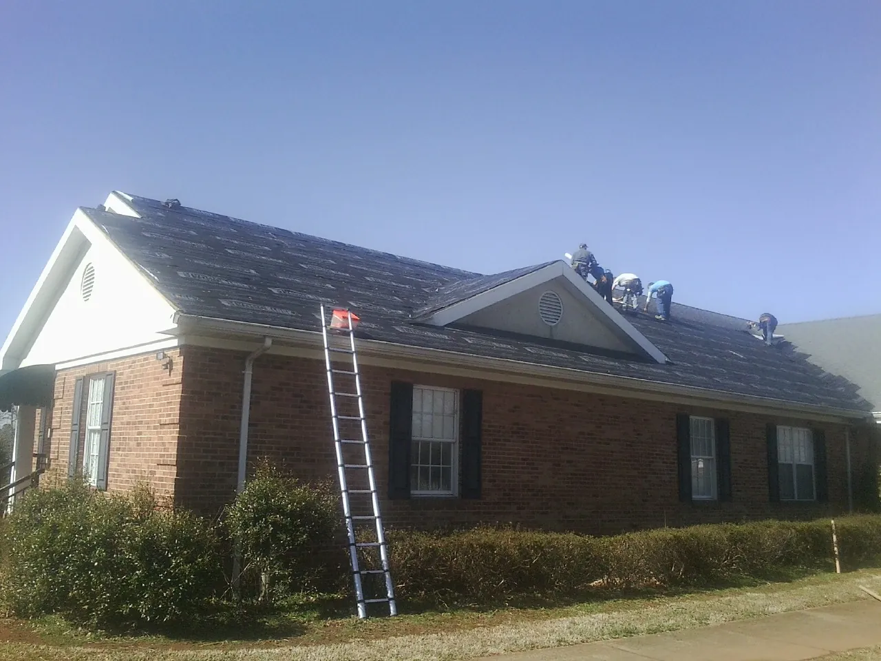 Crew tearing shingles off a brick ranch roof with a ladder set — Metal Roof Repair work by our crew in Saint Marks