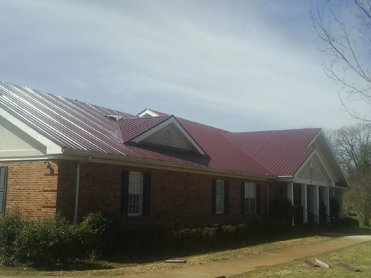 Red metal roof with gabled entries on a long brick building, from a Hail Damage Roof Repair job in Saint Marks