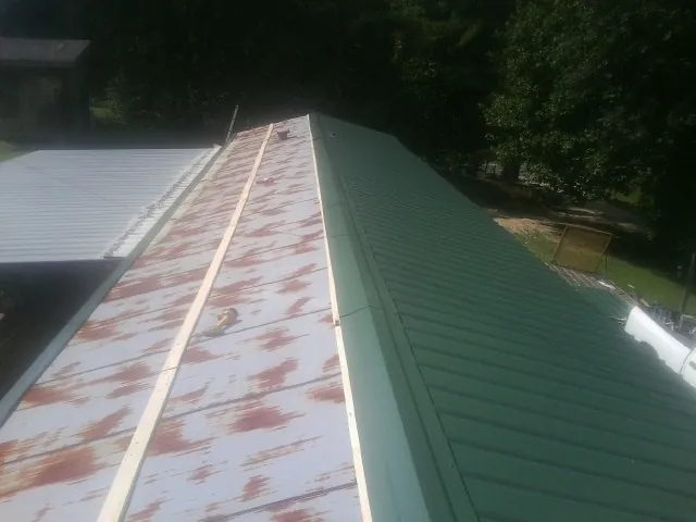 Old rusted panels beside newly installed green metal roofing — Wind Damage Roof Repair by Roofing Brothers in Saint Marks