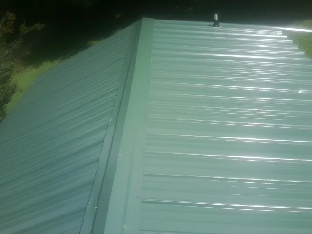 New green metal panels meeting at the ridge of a roof — Flat Roof Repair work by our crew in Saint Marks