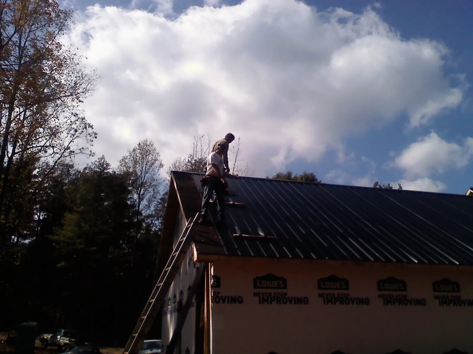 Roofer fastening dark metal panels high against a cloudy sky, from a Roof Inspection job in Saint Marks